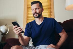 A man sitting on the couch and looking at his smartphone.